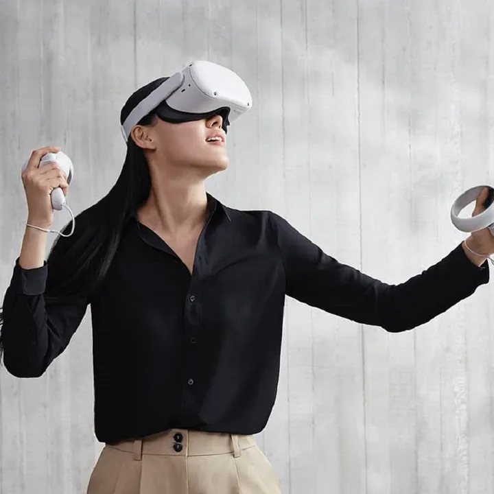 A person wearing and using an Oculus Quest 2 VR headset in front of a gray background.