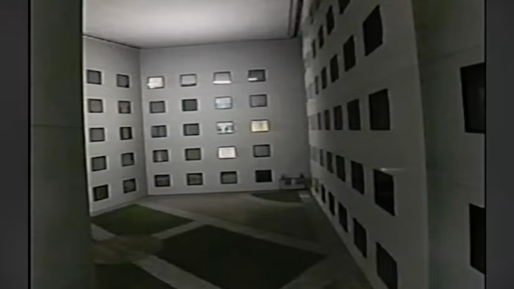 A shot of a strange hotel courtyard with grass on the ground, but with a roof where there should be a sky.