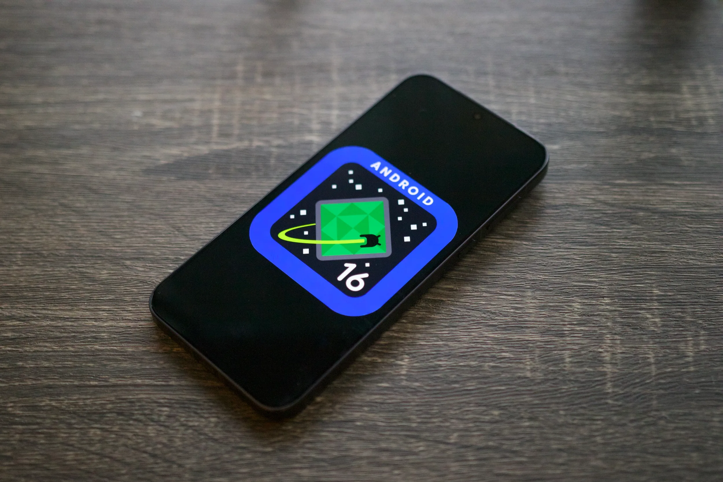 Android 16 logo on a smartphone lying on a shelf.