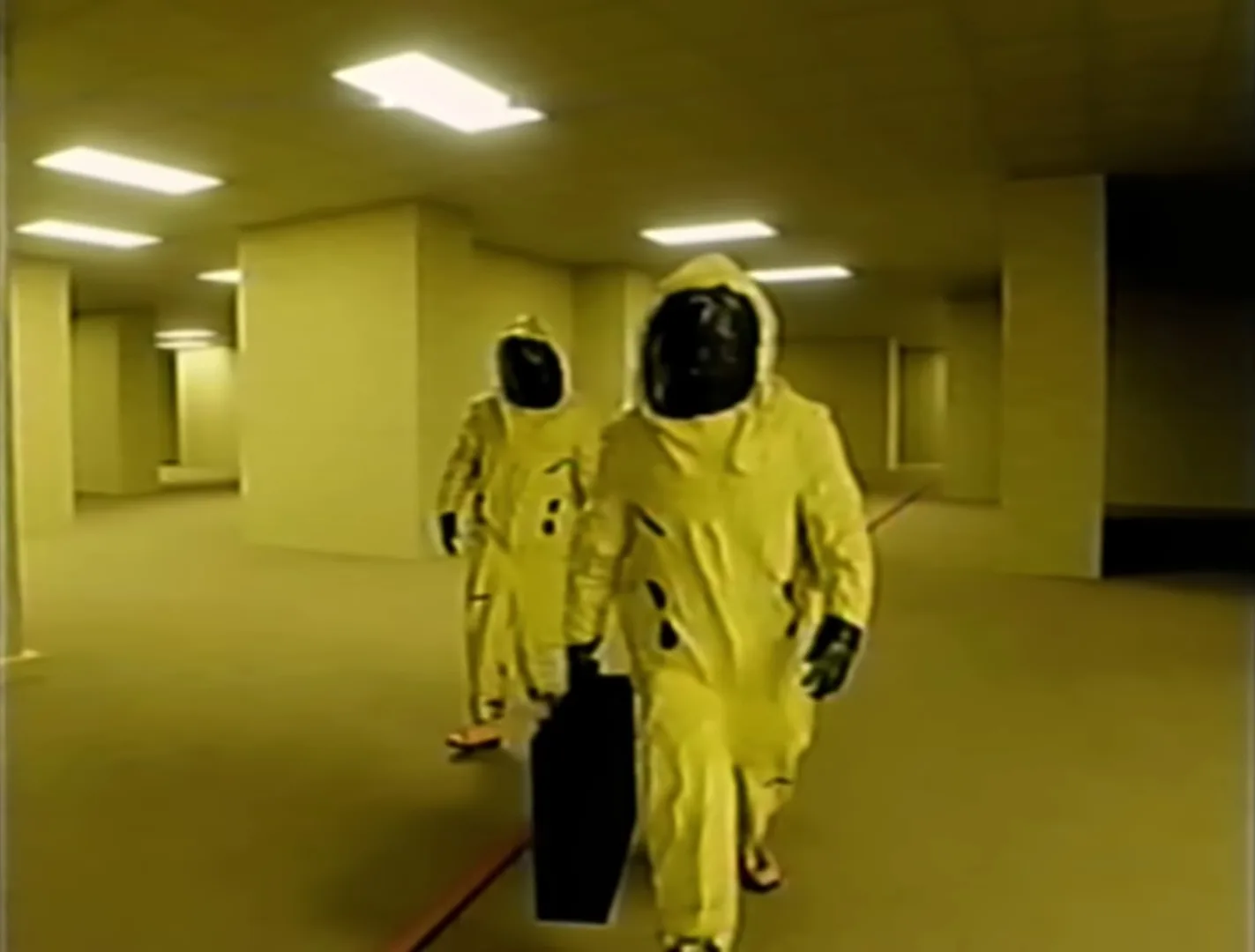 In The Backrooms web series, two people in hazmat suits are walking through a yellow room.