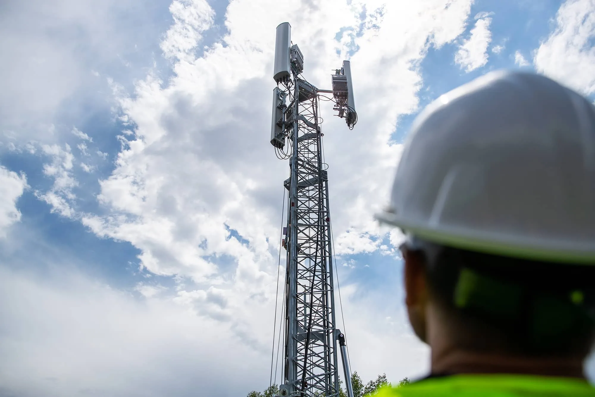 5G vs. LTE: What's the Difference and Why Should You Care? 4 A worker looking up at the 5G tower against a cloudy sky.
