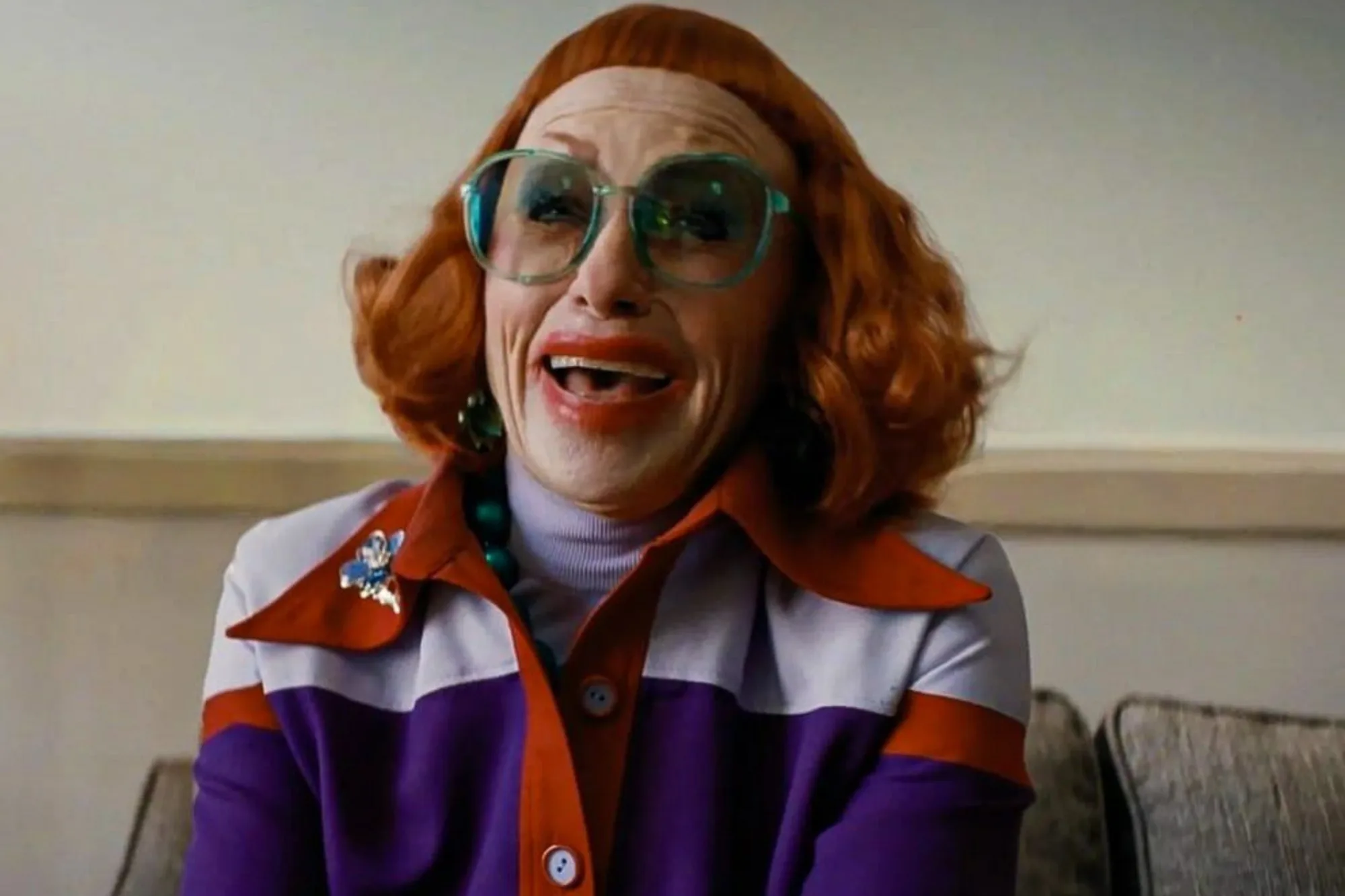 Actress Amy Madigan smiles wearing big glasses and a red wig as she plays Aunt Gladys in Zach Cregger's horror film Weapons.