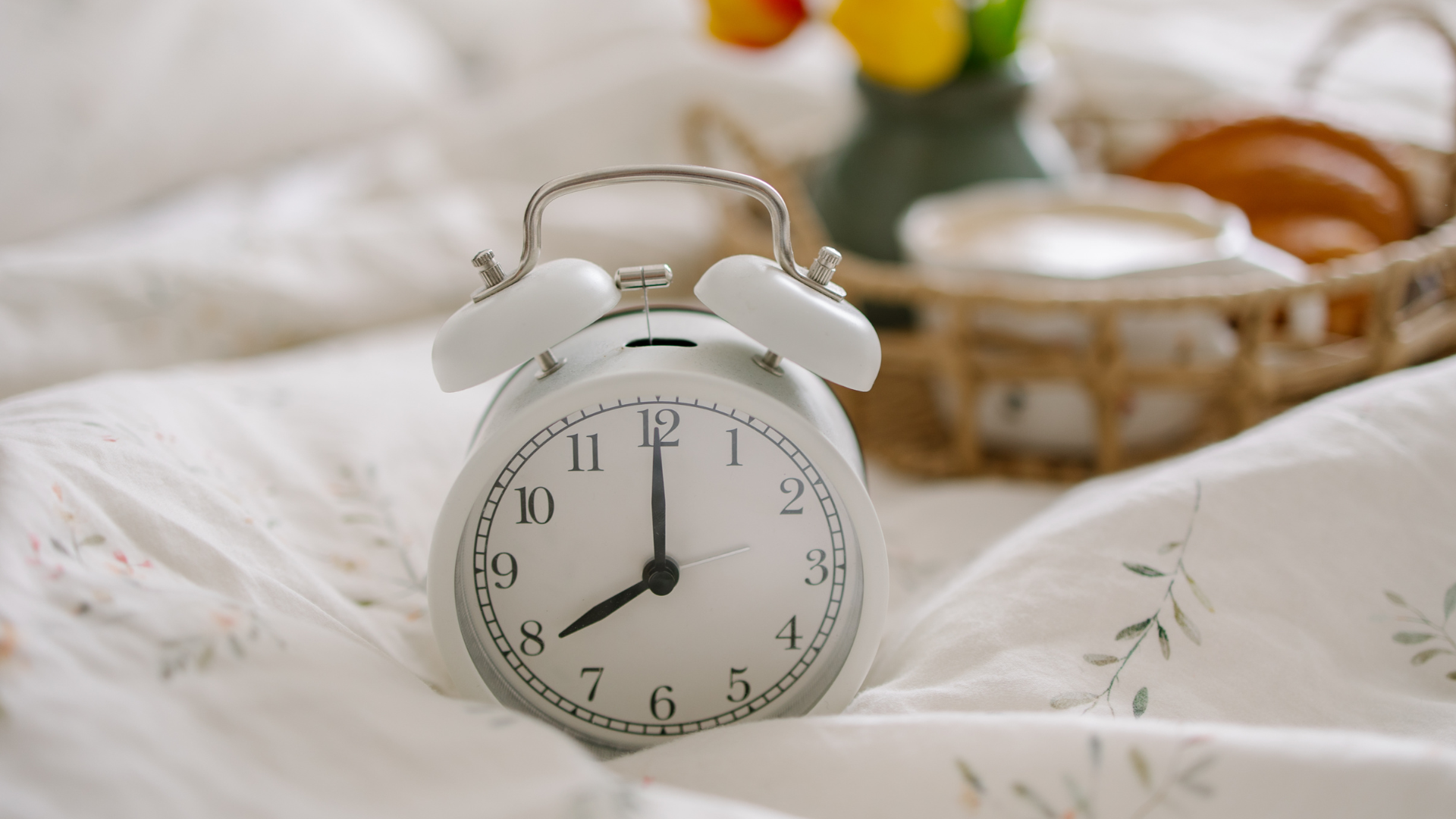 ایک سفید الارم گھڑی دھوپ والے کمرے میں بستر پر پڑی ہے۔