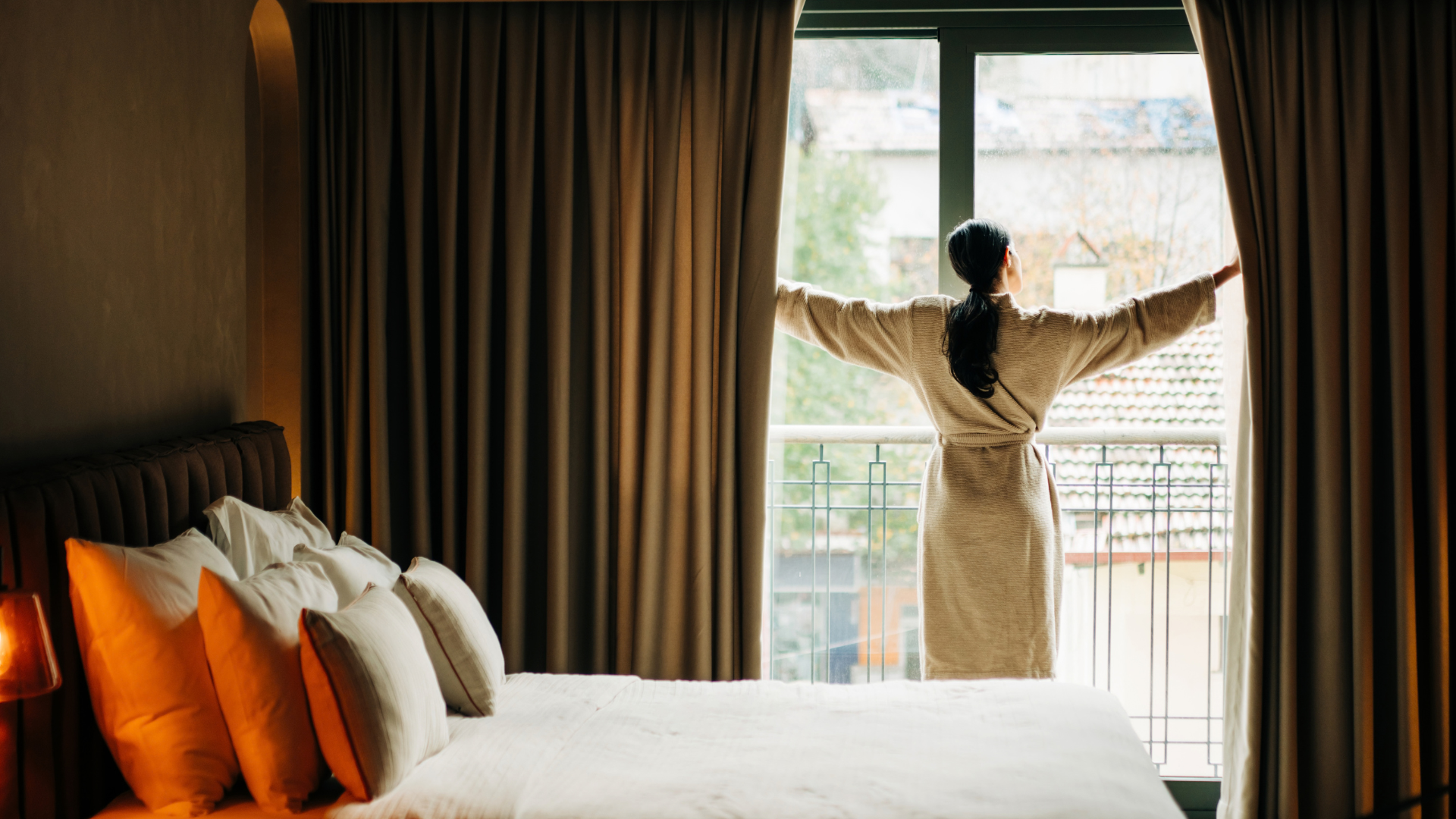 ایک عورت صبح کے وقت اپنے سونے کے کمرے کے پردے کھولتی ہے تاکہ سورج کی روشنی آئے۔