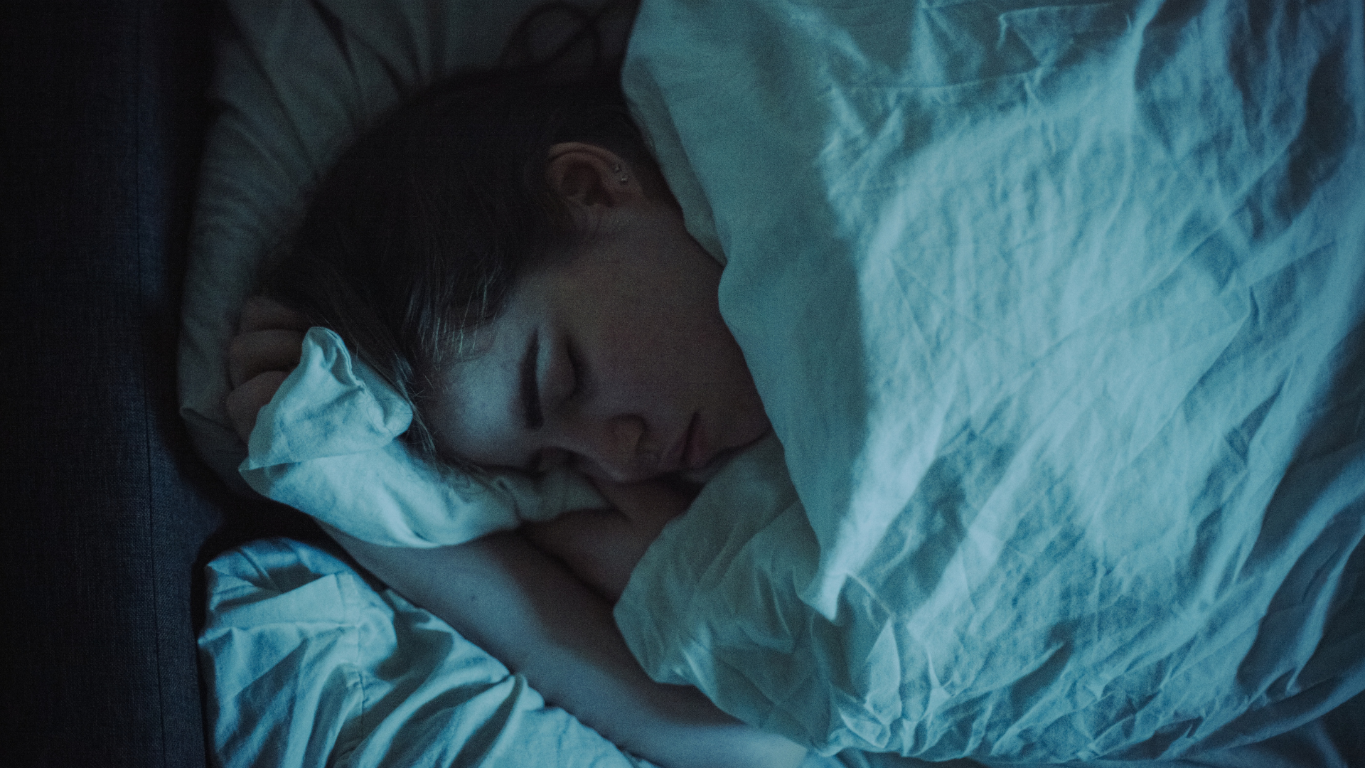 عورت رات کو بستر میں اپنے پہلو کے بل سوتی ہے، بستر سفید بستر سے ڈھکا ہوا ہے۔