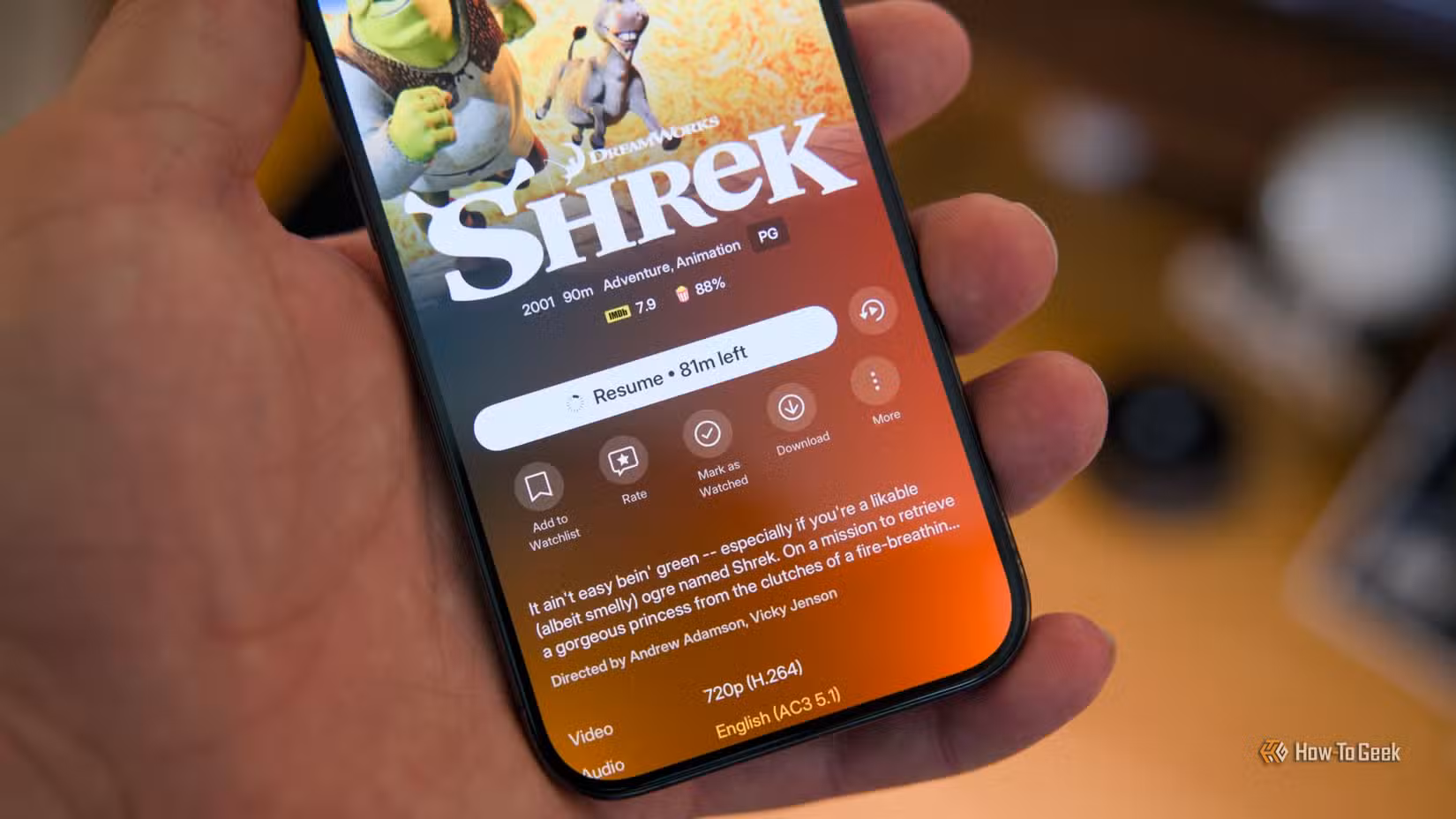 آئی فون 15 پرو ہاتھ میں Plex موبائل ایپ کو ڈاؤن لوڈ آئیکن کے ساتھ دکھا رہا ہے جیسا کہ Shrek فلم میں دیکھا گیا ہے۔