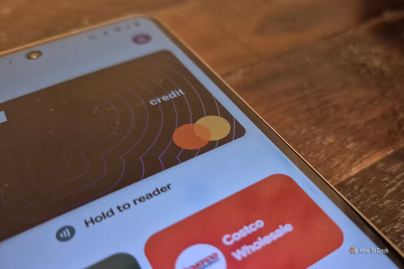 کارڈ آپ کے فون پر Google Wallet ایپ میں کھلتا ہے، جسے لکڑی کی سطح پر رکھا گیا ہے۔ 