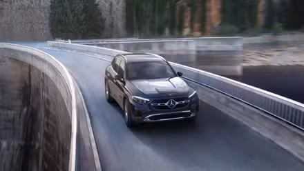 ایک سیاہ 2025 مرسڈیز بینز GLC کا متحرک سامنے کا 3/4 شاٹ ایک پل پر چلا رہا ہے۔