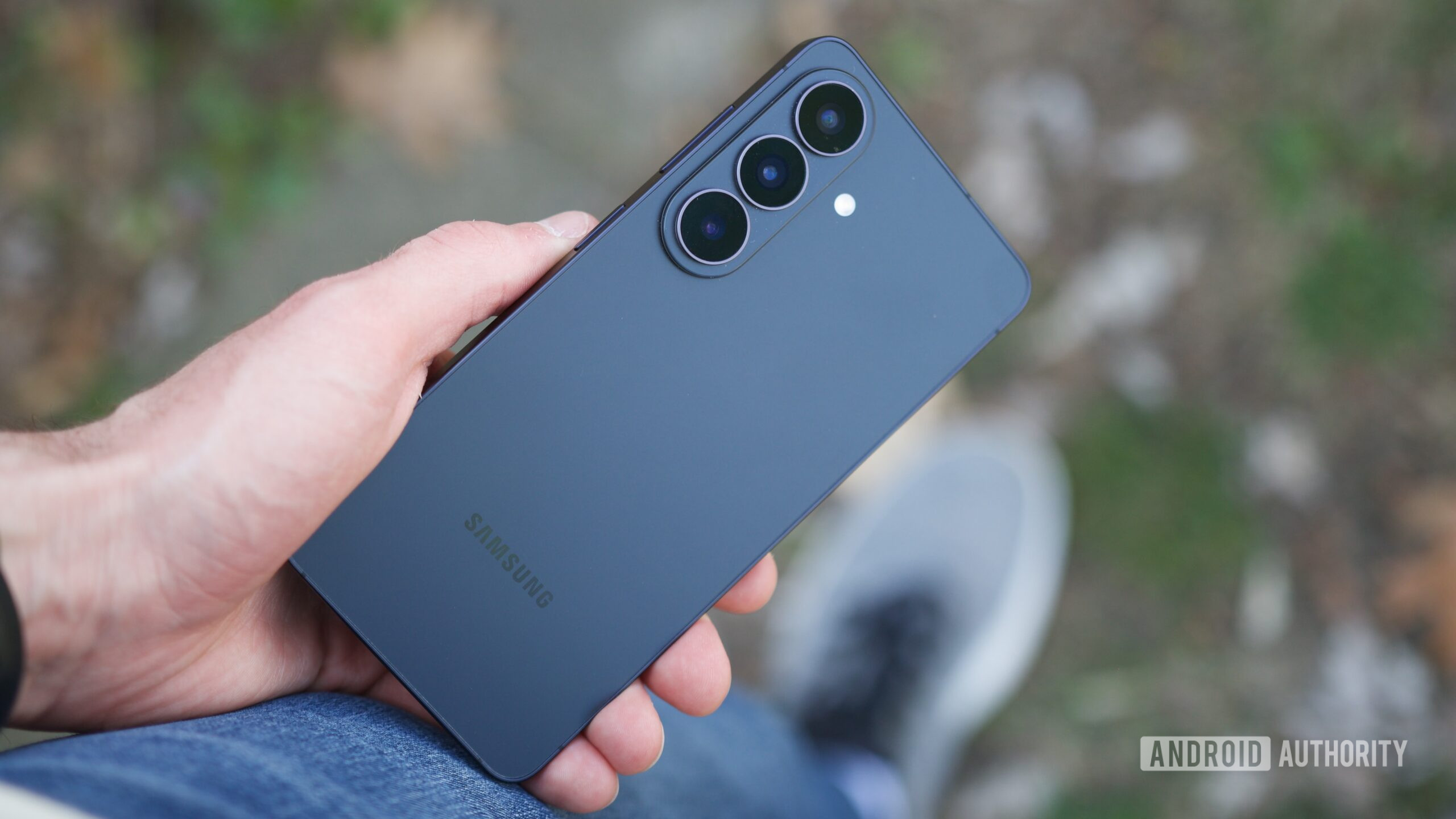 Samsung Galaxy S26 Basic Review Phone Again 4 Galaxy S26 پکڑے ہوئے کوئی شخص فون کا پچھلا حصہ دکھا رہا ہے۔